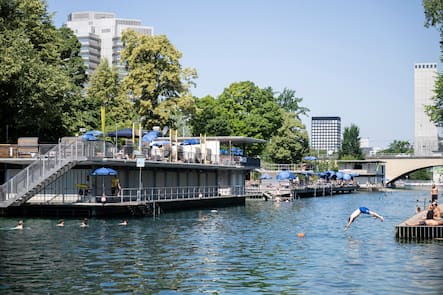 Menschen geniessen an einem Hitzetag die Sonne und schwimmen in der Limmat beim Flussbad Oberer Letten, am Freitag, 19. Juni 2026 in Zuerich. Seit Donnerstag gibt der Bund Hitzewarnungen der Stufen 3 und 4 heraus. Diese Warnungen gelten bis naechsten Dienstag. Laut MeteoSchweiz ist das Ende der Hitzewelle derzeit noch offen. (KEYSTONE/Andreas Becker)