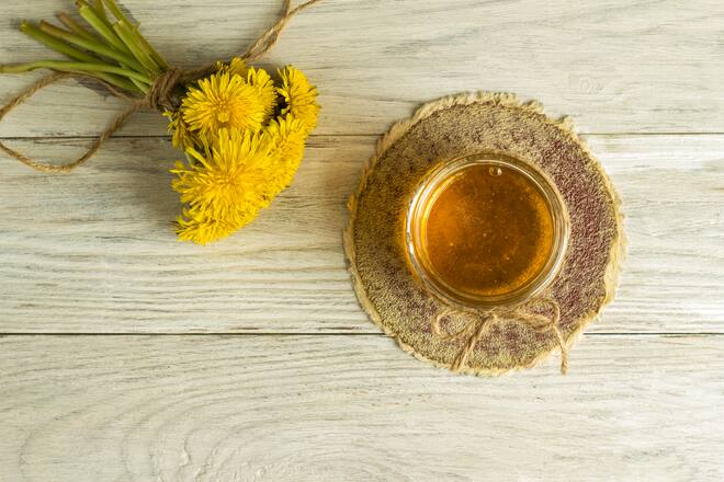 Homemade delicious dandelion jam on a light wooden table with yellow dandelions. Dandelion flower syrup. Useful preservation for the winter.