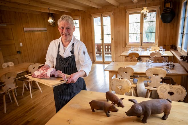 Mann in rustikaler Wirtsstube präsentiert Fleischplatte
