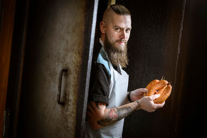 Le boucher Michaël Wyler pose avec ses saucissons vaudois et des saucisses aux choux dans sa boucherie, mardi 12 décembre 2023 à Lucens. (© Gabriel Monnet)