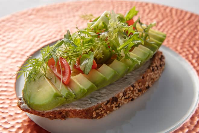 Getoastetes Vollkornbrot, belegt mit Kräuterquark, Tomaten, Avocado, Agrvensirip und Mikrokräuern.