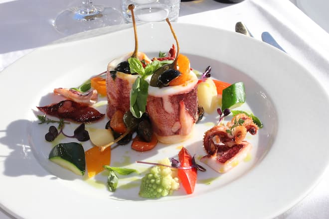 Goldbraun gebackene Tintenfischringe mit Kapernblueten schwarzen Oliven Tomatenstueckchen und Basilikumoel Rene Nagy