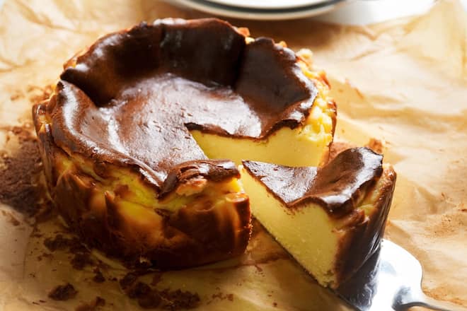 Gluten free basque burnt cheesecake on a brown baking paper next to white round saucers.