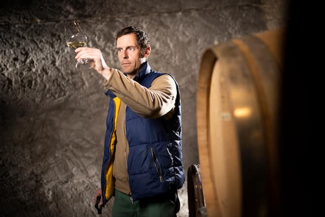 Le vigneron Steve Bettschen, pose dans sa cave avec un verre de vin blanc à la main, le mardi 15 février 2022 à La Sarraz. (© Gabriel Monnet/ Gault & Millau)