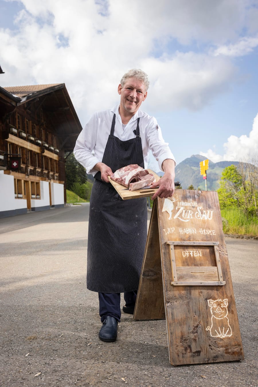 älterer Mann mit Fleischplatte vor einem Berggasthaus