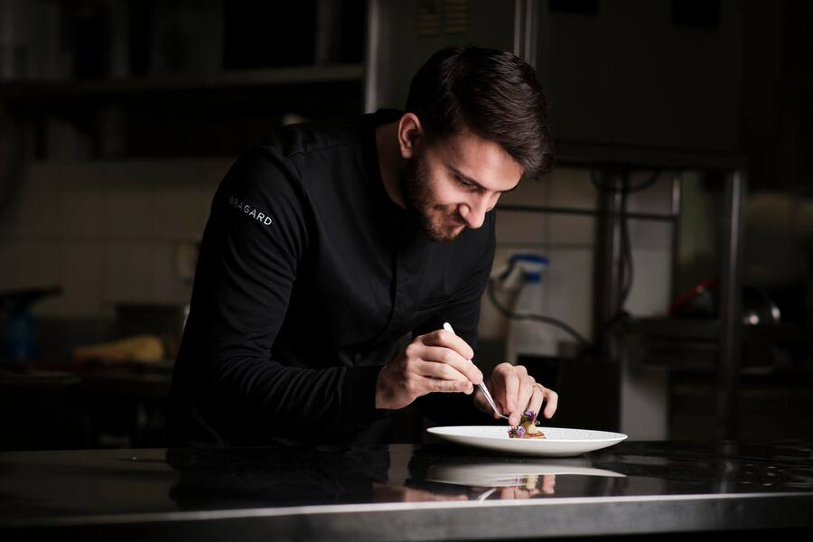 Junger Mann in schwarzer Kochbluse richtet einen Teller an