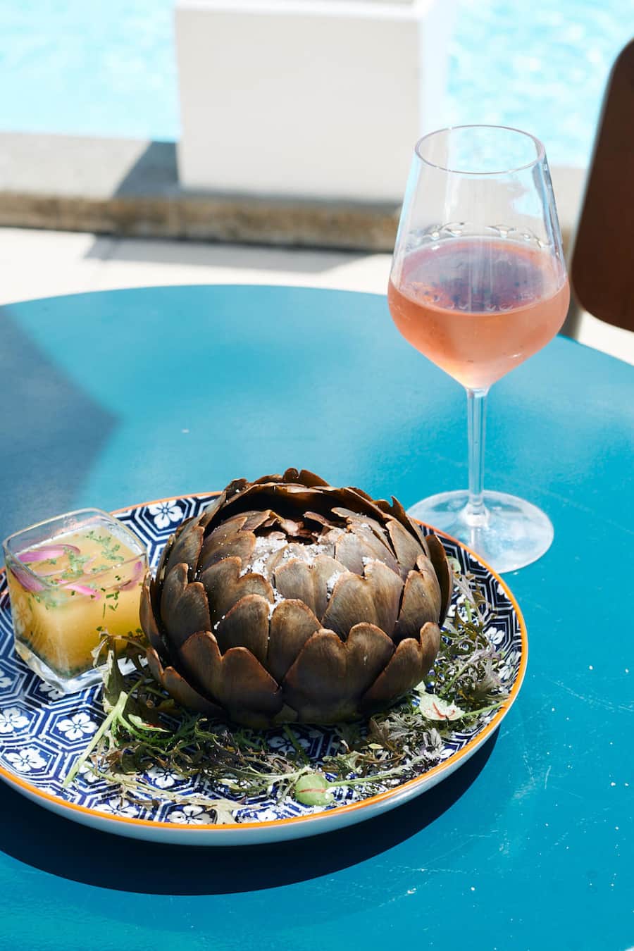 Artischocke auf blauem Tisch mit einem Glas Roséwein