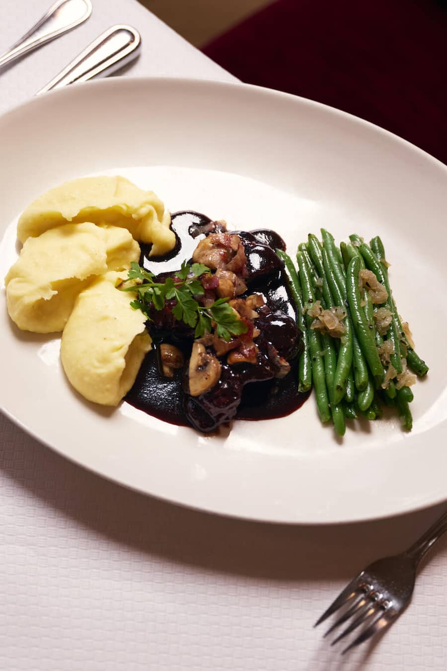 oq au Vin, Schweizer Poulet, Rotweinsauce, Kartoffelstock und Bohnen