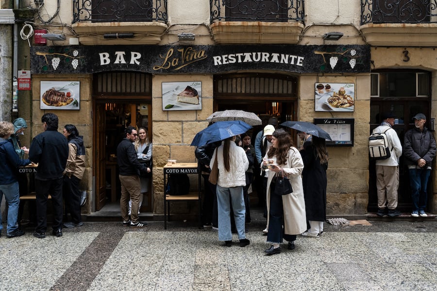 Customers wait in the rain outside La Viña restaurant in San Sebastián, Spain, May 14, 2026. Santiago Rivera, owner of La Viña, is widely credited with creating the "burnt" Basque cheesecake in the 1980s, though he doesn't love the spinoffs it has spawned. Decades later, he's preparing to hand over his kitchen to his children. (Markel Redondo/The New York Times)