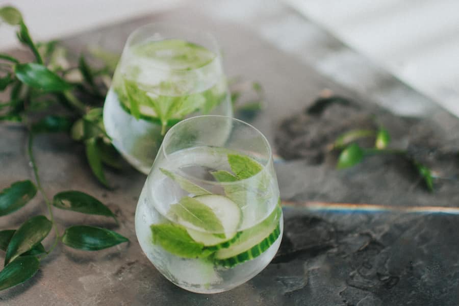 Cold, refreshing glass of clear liquid, Gin and tonic or water, garnished with mint and cucumber, on a stylish concrete surface. Space for copy.